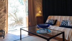 Una habitación con una mesa de centro de vidrio, un sofá con cojines estampados, una lámpara y vistas a un espacio exterior a través de una puerta.