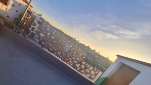 En terrass med utsikt över ett avlägset landskap, en byggnad med en grön och vit fasad och en trädörr.