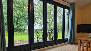 A room with large windows, a wooden table, and a television. - Lily's Cottage Suffolk Sleeps 2 With Pets (Stowmarket)
