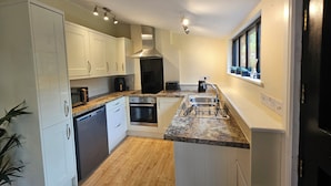 A compact kitchen with white cabinets, a stainless steel range hood, a built-in oven, and a granite countertop. - Lily's Cottage Suffolk Sleeps 2 With Pets (Stowmarket)