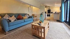 A modern living room with a blue sofa, a wooden coffee table, and a kitchen in the background. - Lily's Cottage Suffolk Sleeps 2 With Pets (Stowmarket)