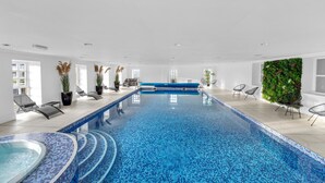A modern indoor swimming pool with clear blue water, surrounded by lounge chairs and a green vertical garden wall. - Hunter Oak Retreat, Indoor heated pool, Sauna, Hot Tub Sleeps 30 (Burnley)