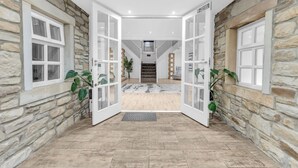 A spacious hallway with stone walls, white-framed glass doors, and a wooden floor leading to a staircase. - Hunter Oak Retreat, Indoor heated pool, Sauna, Hot Tub Sleeps 30 (Burnley)