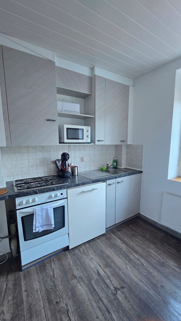 Una cocina con armarios blancos, microondas, estufa a gas y piso de madera.