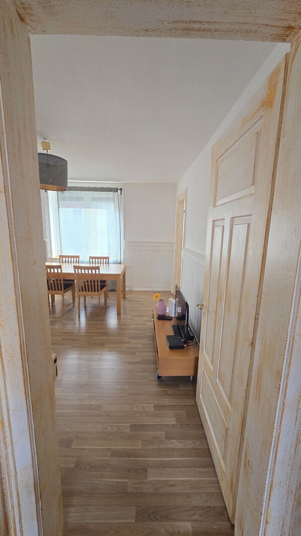 A room with a wooden floor, a dining table with chairs, a lamp, and a door with a handle.