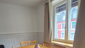 A dining room with a wooden table, chairs, a vase with a flower, and a window with curtains. - Charming 2-bedroom apartment in vibrant Zürich with WiFi (Zürich)