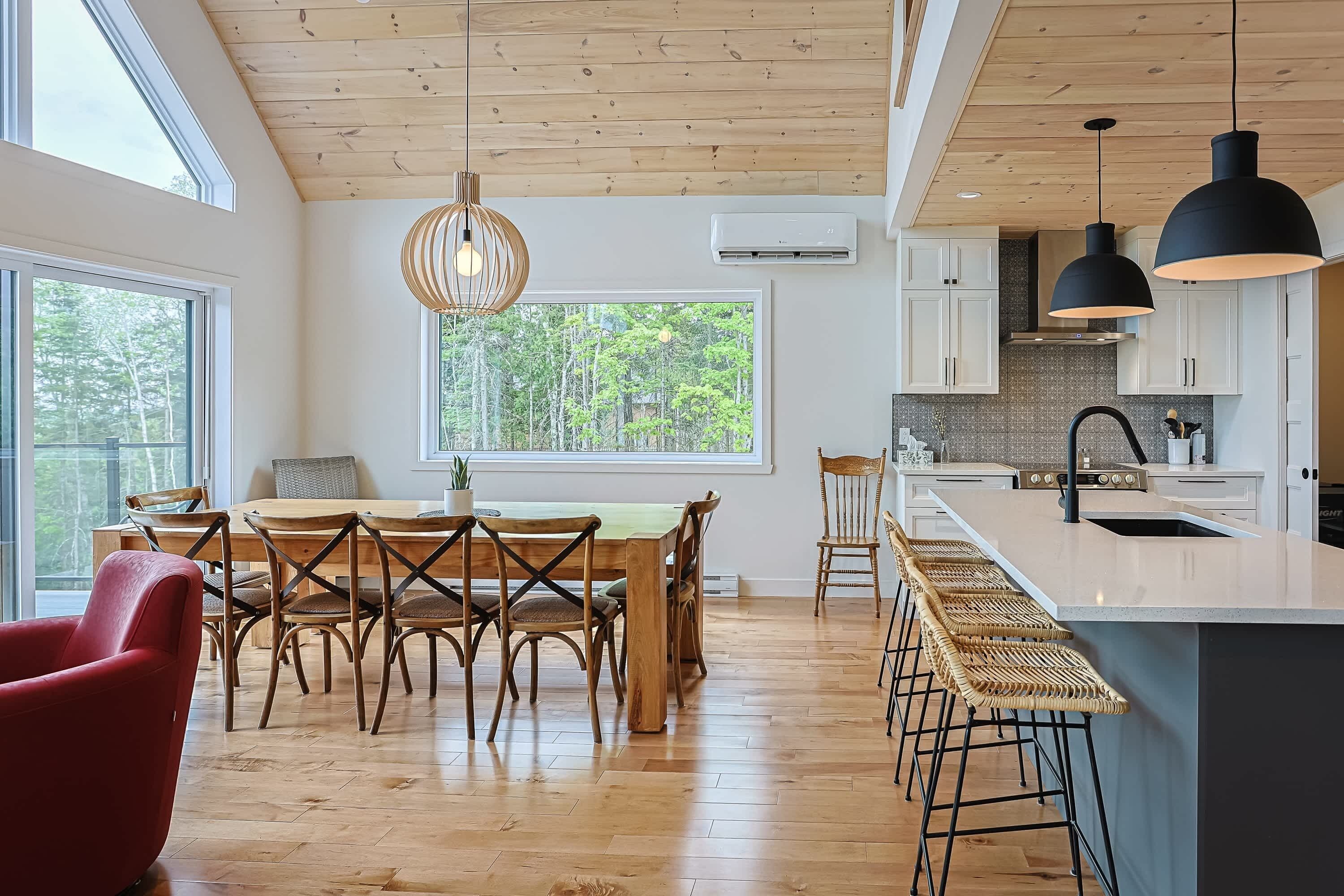 Una cocina moderna con pisos de madera, un comedor con una mesa y sillas de madera, y un amplio ventanal con vistas a la vegetación.