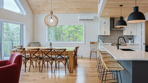 Een moderne keuken met houten vloeren, een eethoek met een houten tafel en stoelen, en een groot raam met uitzicht op groen.
