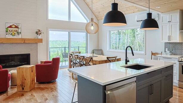 Een moderne keuken met een groot eiland, houten vloeren en een eetgedeelte met rode stoelen.