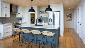 Een moderne keuken met witte kasten, een centraal eiland met barkrukken, roestvrijstalen apparatuur en hanglampen.