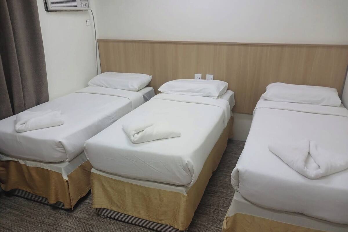 A hotel room with three single beds, each with white bedding and a folded towel.