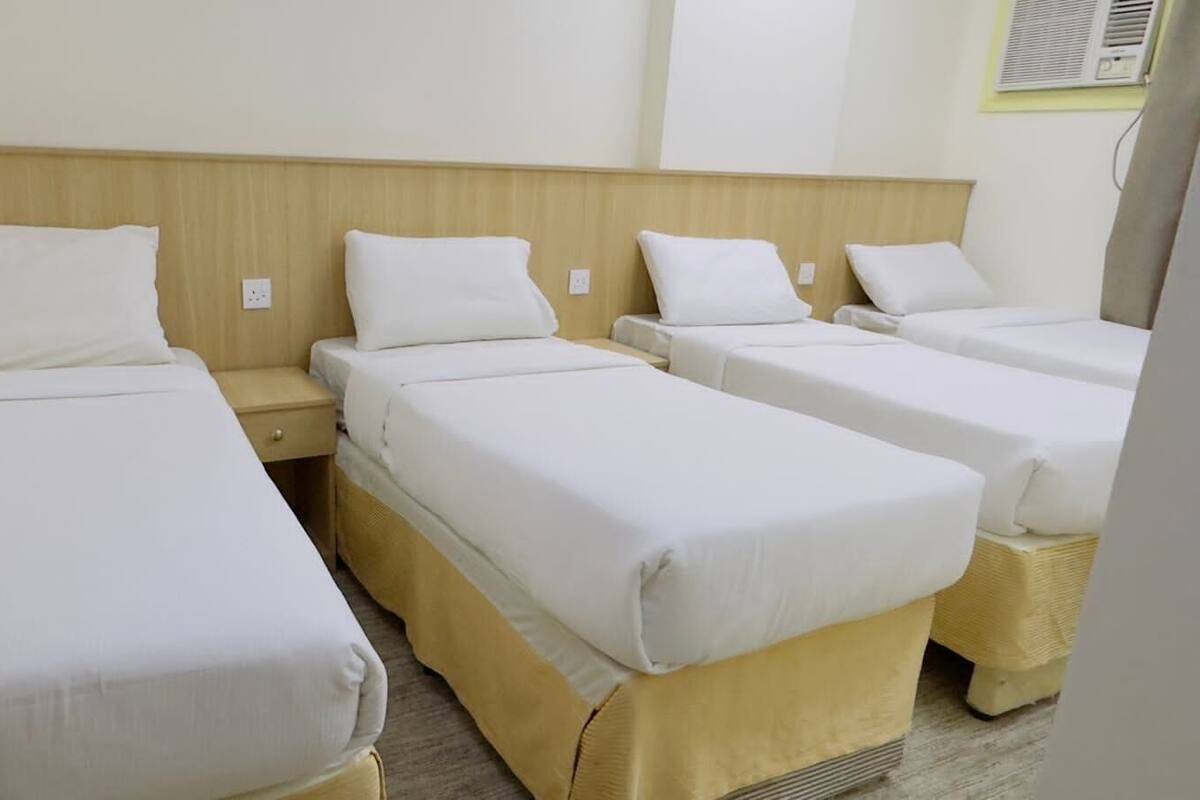 A hotel room with four single beds arranged in a row, each with a wooden headboard and white bedding.