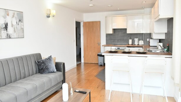 Eine moderne Wohnung mit grauem Sofa, einer Küche mit weißen Schränken und einem Essbereich mit Barhocker.