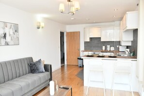 A modern apartment with a grey sofa, a kitchen with white cabinets, and a dining area with bar stools.