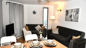 Ein modernes Wohnzimmer mit einem schwarzen Sofa, einem Holzessttisch mit Schüsseln und Essstäbchen, einem Fernseher und einem Gemälde an der Wand.