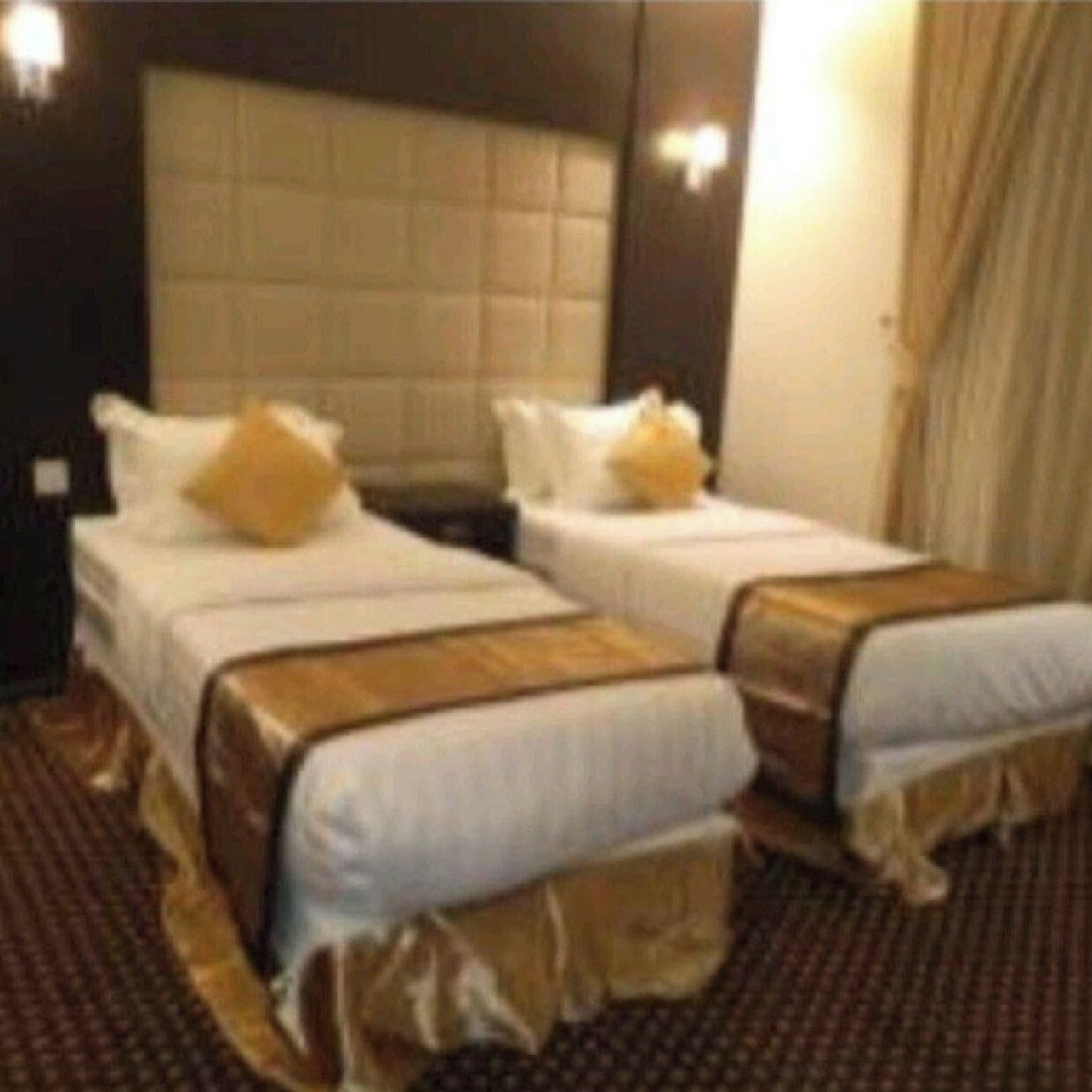 Une chambre d’hôtel avec deux lits, chacun doté d’une tête de lit, de draps blancs et d’un élément décoratif de couleur marron.