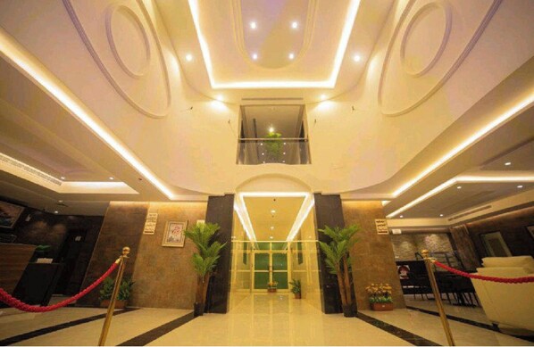 A hotel lobby with a modern design, featuring a central reception desk, a staircase, and potted plants.