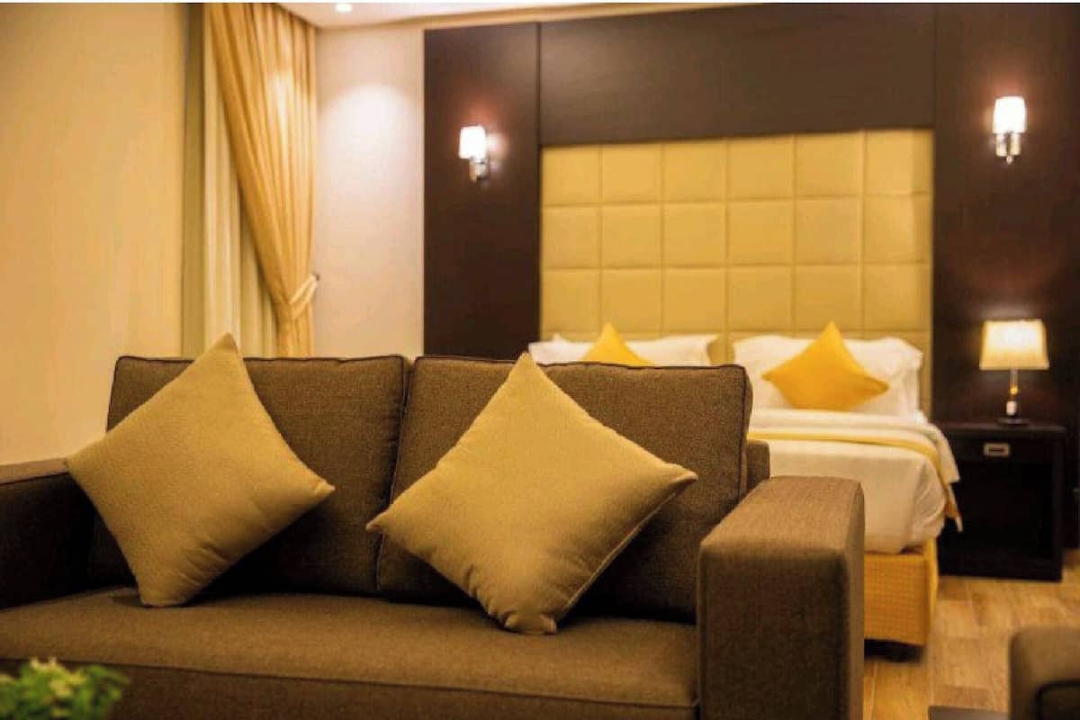 A hotel room with a sofa, a bed with yellow pillows, and two wall sconces.