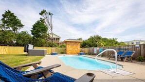 Un giardino con piscina, poltrone da relax e un pontile in legno.
