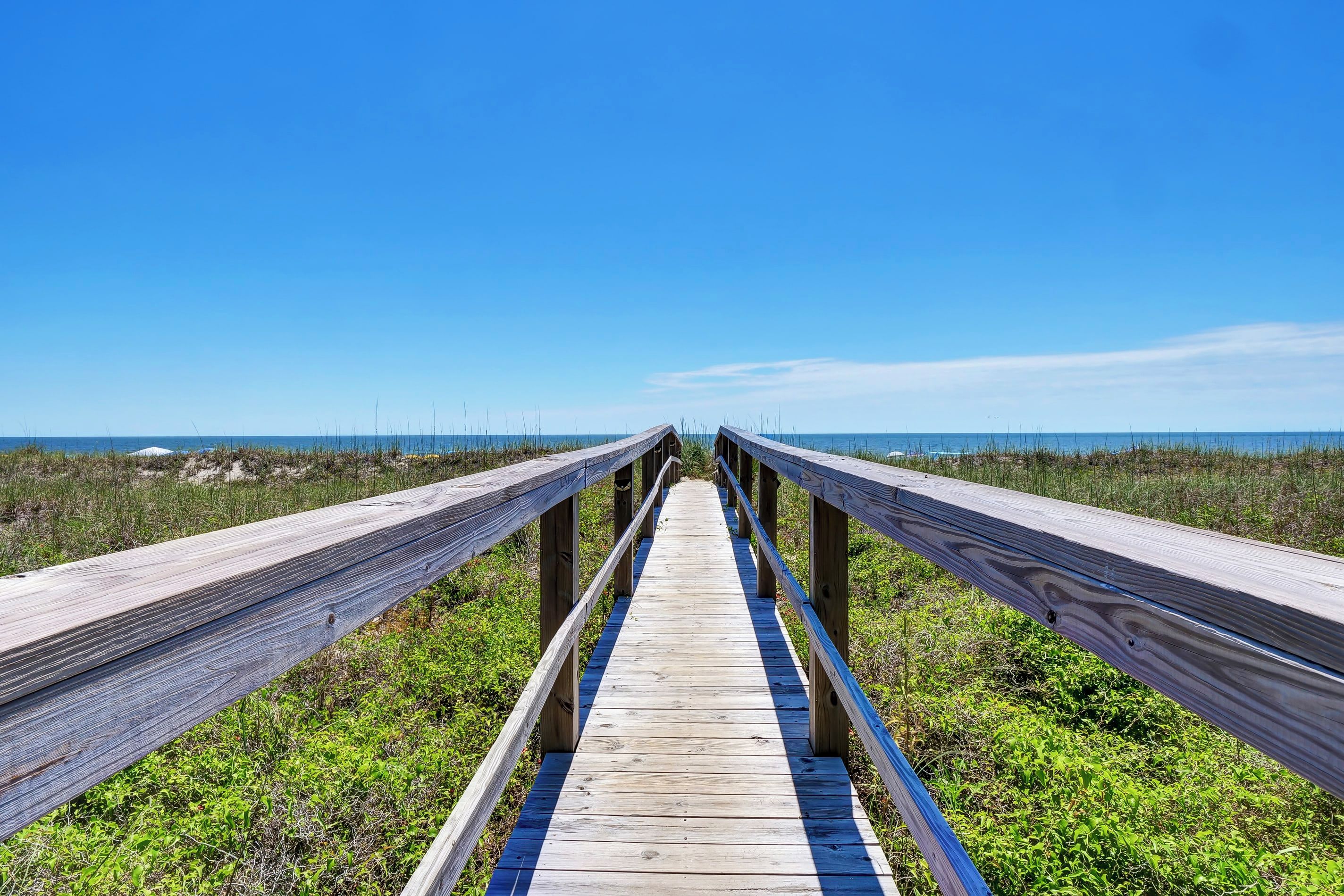 A wooden boardwalk leading to a beach with a clear sky.