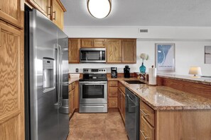 A modern kitchen with stainless steel appliances, wooden cabinets, and a granite countertop.