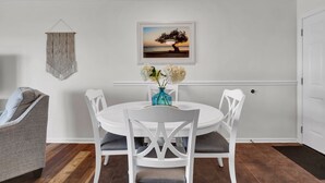 A dining area with a white table and chairs, a vase with flowers, and a framed picture on the wall. - Infinity Summer, Oceanfront Retreat (Carolina Beach)