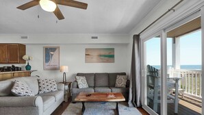 A living room with a sofa, a coffee table, and a large window with a view of the ocean. - Infinity Summer, Oceanfront Retreat (Carolina Beach)