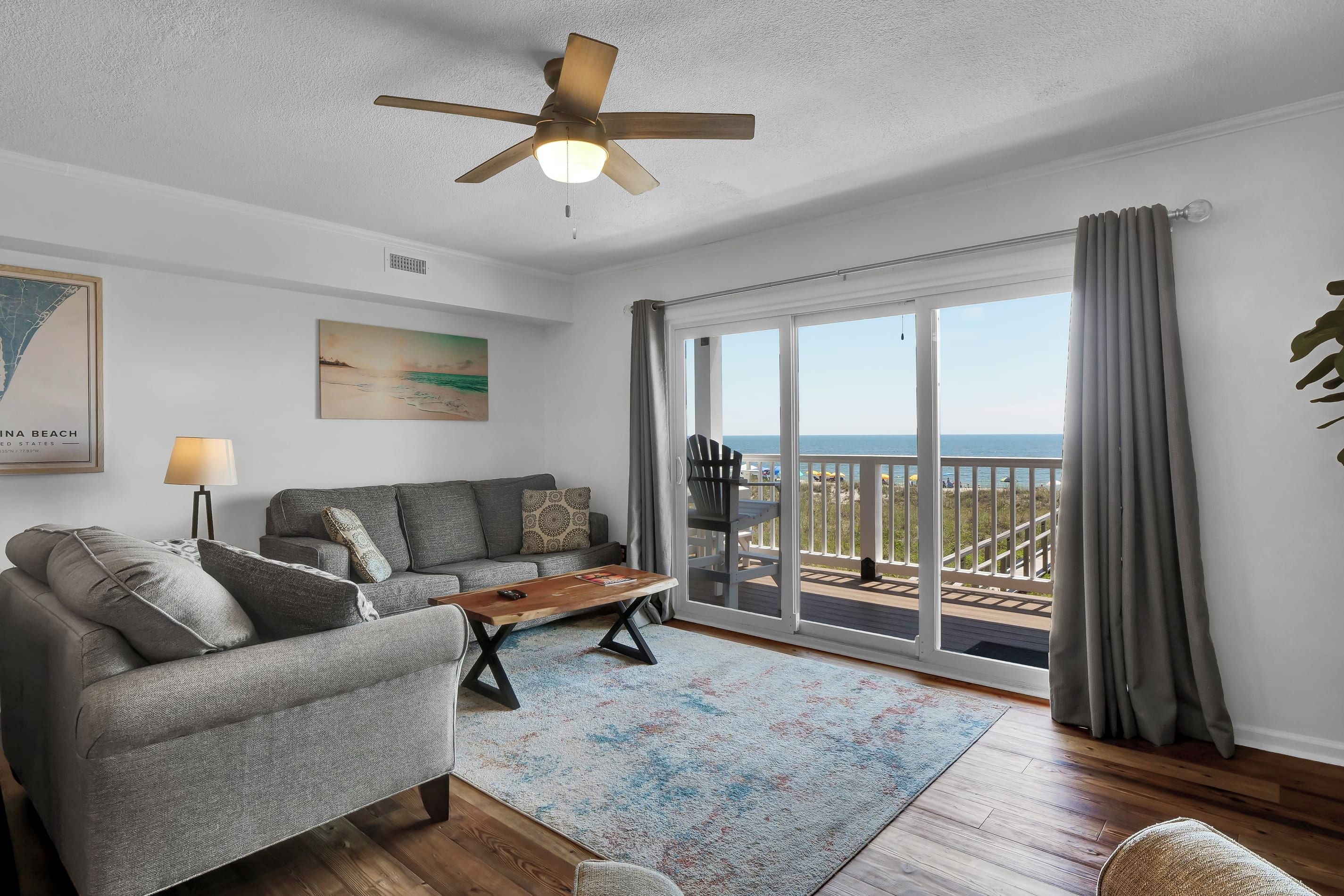 Un salon spacieux doté d’un ventilateur de plafond, d’un ensemble de canapés, d’une table basse et offrant une vue sur la plage grâce à de grandes portes-fenêtres coulissantes.