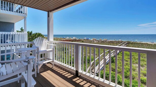 A wooden deck with white railings and chairs overlooking a beach with umbrellas and people. - Infinity Summer, Oceanfront Retreat (Carolina Beach)