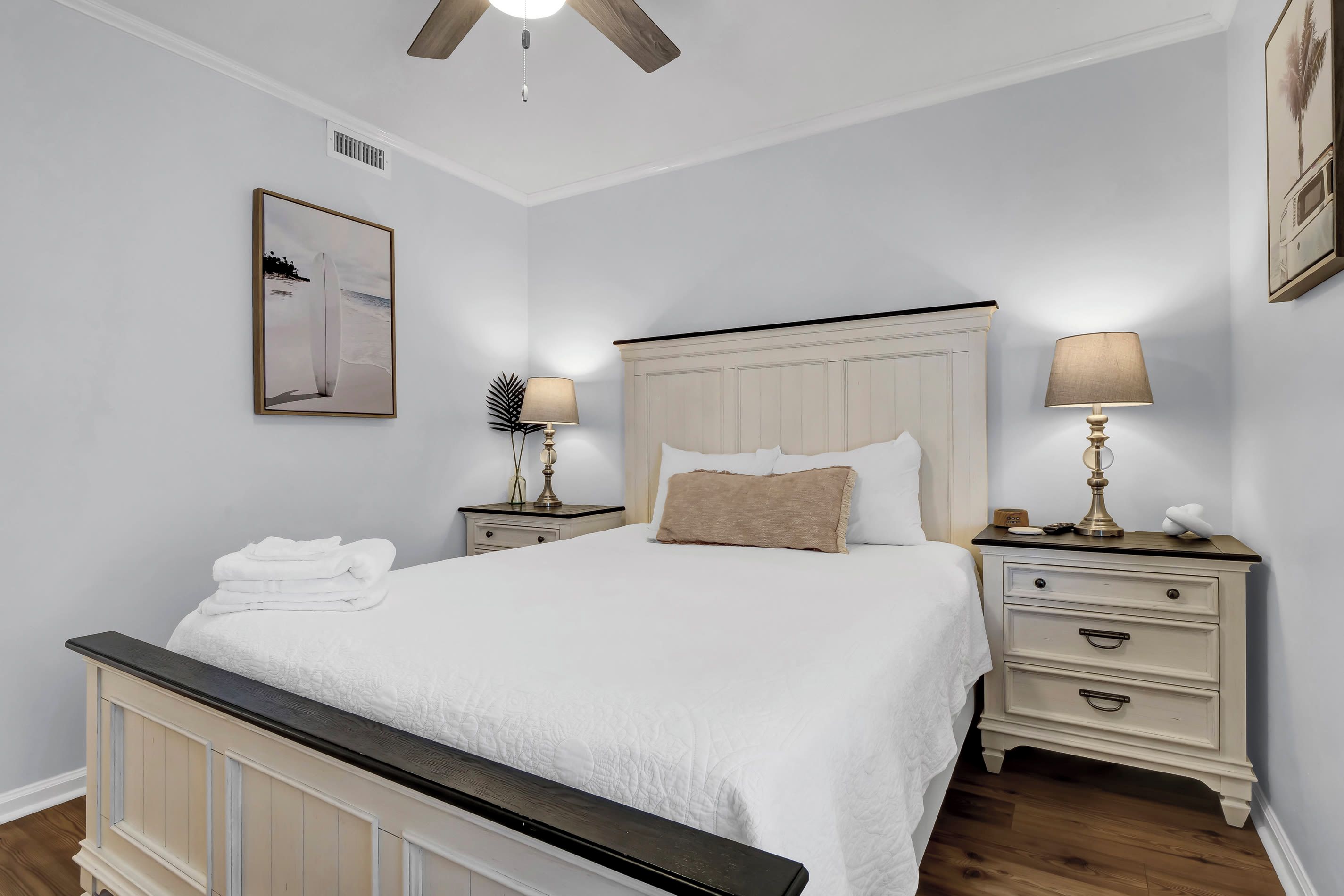 A bedroom with a bed, nightstands, a ceiling fan, and a framed picture on the wall.