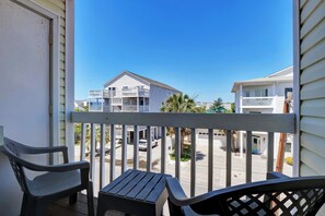A balcony with two chairs, a view of a residential street, and a clear blue sky.