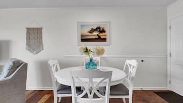 Un comedor con una mesa y sillas blancas, un jarrón con flores y un cuadro en la pared.