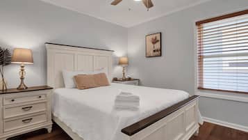 Ein Schlafzimmer mit einem Bett, zwei Nachttischen, einem Deckenventilator, einem Fenster mit Jalousien und einem Wandbild.