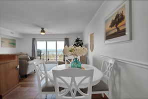 A dining area with a round table, white chairs, a vase with flowers, and a painting on the wall.