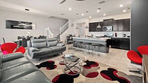 A modern living room with a gray sofa, red chairs, a coffee table, and a kitchen area with dark cabinets and a white countertop. - Townhouse w/ pool & resort water park (Davenport)