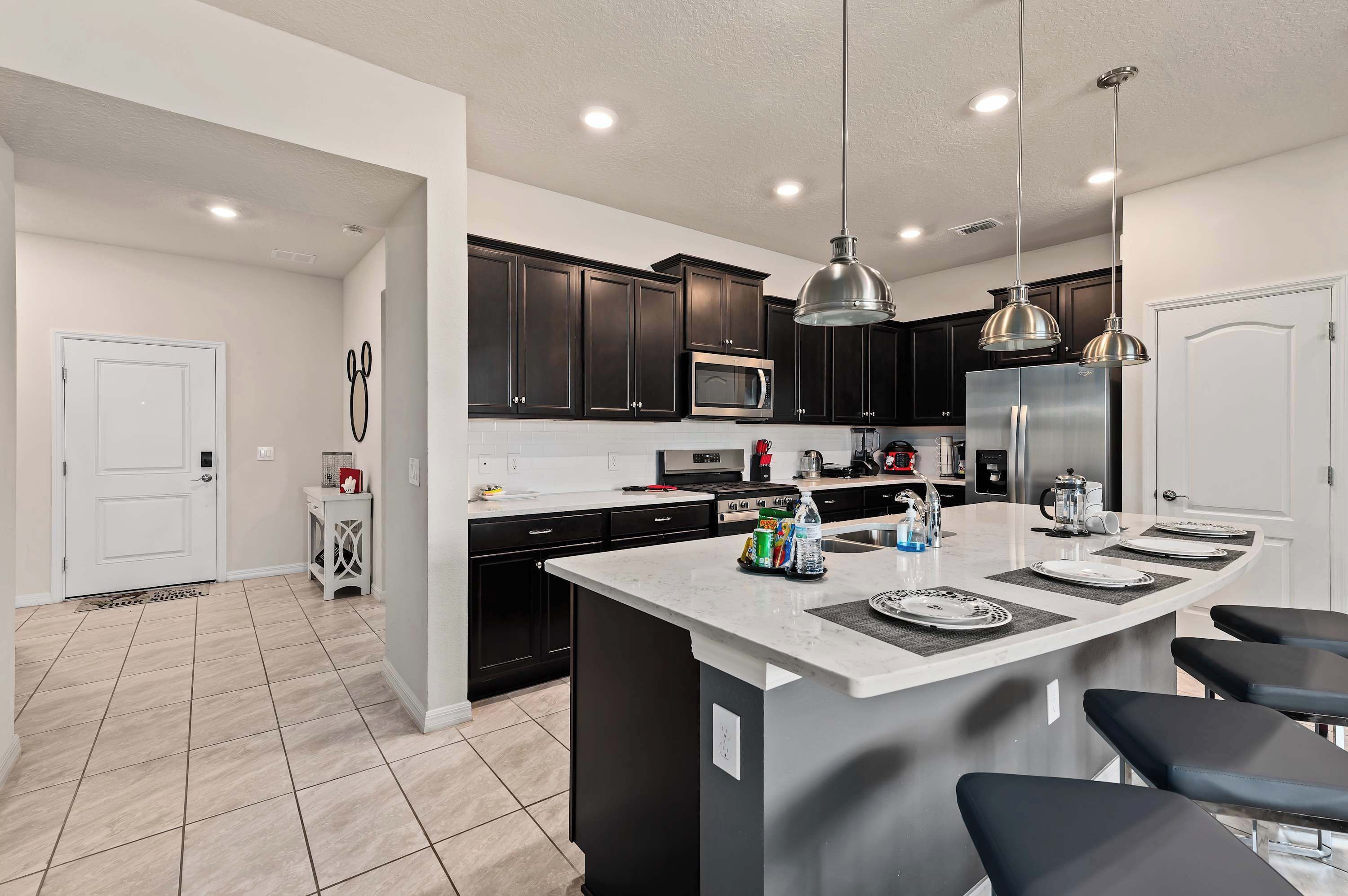 A modern kitchen with dark cabinets, a central island with bar stools, stainless steel appliances, and pendant lighting.