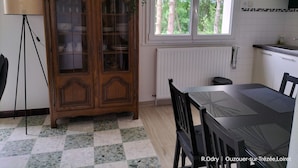 A dining area with a wooden cabinet, a table with chairs, a window with a view of trees, and a radiator.
