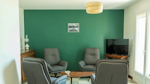 A living room with two grey armchairs, a small coffee table, a television on a wooden stand, and a green wall with a picture.
