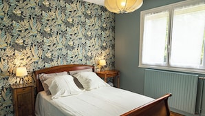 A bedroom with a floral wallpaper, a wooden bed, two bedside tables with lamps, and a window with a view.
