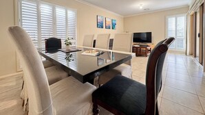 Un coin repas avec une table en verre, des chaises rembourrées, un téléviseur et des œuvres d’art accrochées au mur.
