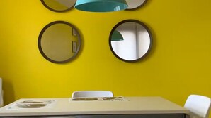 A dining area with a yellow wall, four round mirrors, and a teal pendant light. - Apartamento Para 4 Personas en Playa Jardín Boiro, Puerto de Escarabote (Boiro)