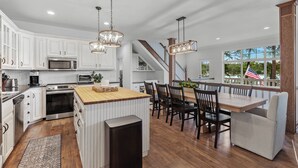 Una cocina amplia con armarios blancos, una isla de madera y un comedor con vistas al exterior.
