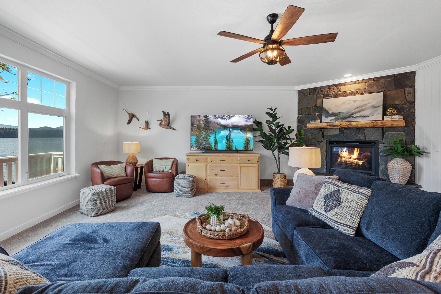 A living room with a fireplace, a ceiling fan, a television, and a view of the outdoors.