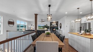 Un comedor amplio con una mesa y sillas de madera, una cocina con armarios blancos y vistas a un lago a través de grandes ventanales.