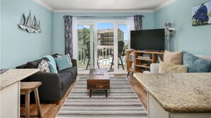 Una sala de estar con sofá, mesa de centro, televisor y vistas al exterior.