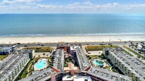 Un hotel frente al mar con varias construcciones, una piscina y vistas a la playa.