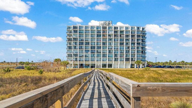 Een modern hotel met een meerlaags gebouw, een houten vlonder die naar de ingang leidt en een helder uitzicht op het omliggende landschap.