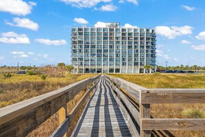 A modern hotel with a multi-story structure, a wooden boardwalk leading to the entrance, and a clear view of the surrounding landscape.