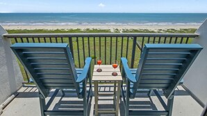 Een balkon met twee blauwe stoelen en een kleine tafel, met uitzicht op een strand en de oceaan op de achtergrond.