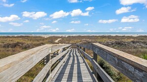 Een houten looppad dat naar een strand leidt, met een heldere lucht en verre horizon.